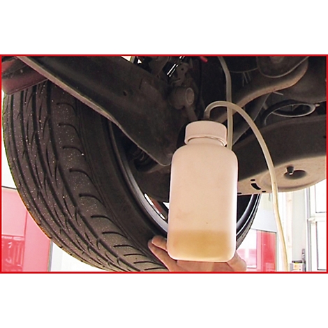 Nahaufnahme des Unterbodens eines Autos mit einem Rad. Eine Flasche wird für die Wartung benutzt.